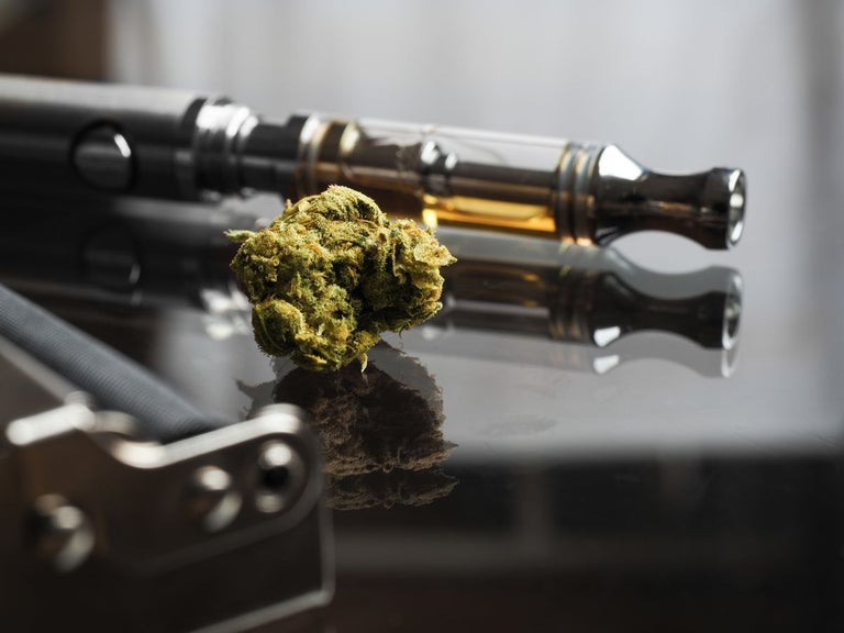 Vape with honey oil and cherry oil inside, placed next to a cannabis bud.