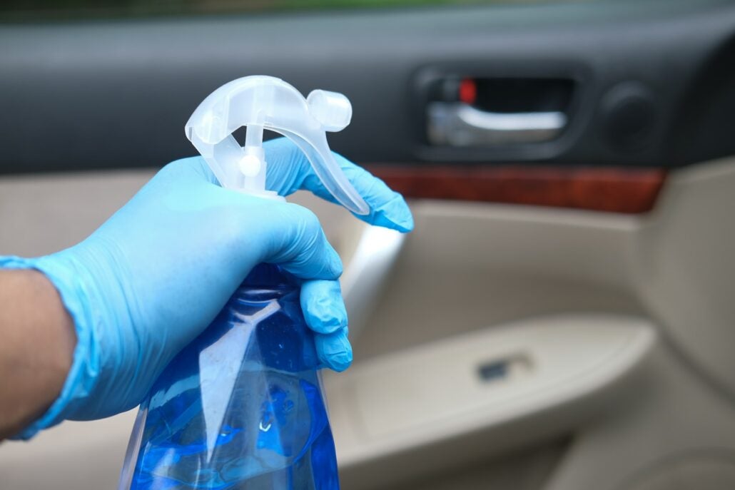 A guy wearing a blue glove spraying car with neutralizing spray inside car. 