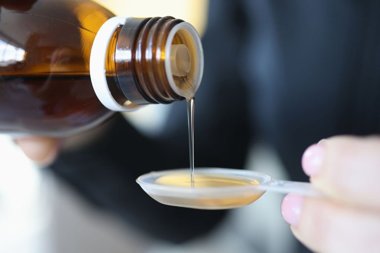 THC syrup poured from a bottle onto a plastic spoon. The substance looks like transparent orange cough syrup.