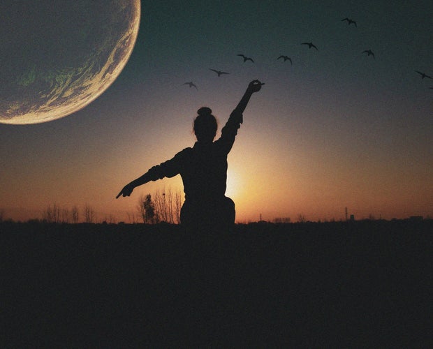 Picture of person standing in an open field with the moon showing up on the left side of the picture.