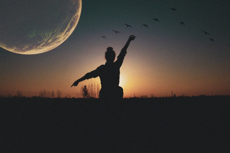 Picture of person standing in an open field with the moon showing up on the left side of the picture.