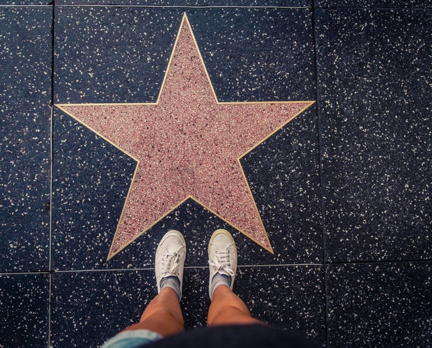 A picture of a person with white shoes standing in front of a star on Hollywood boulevard.