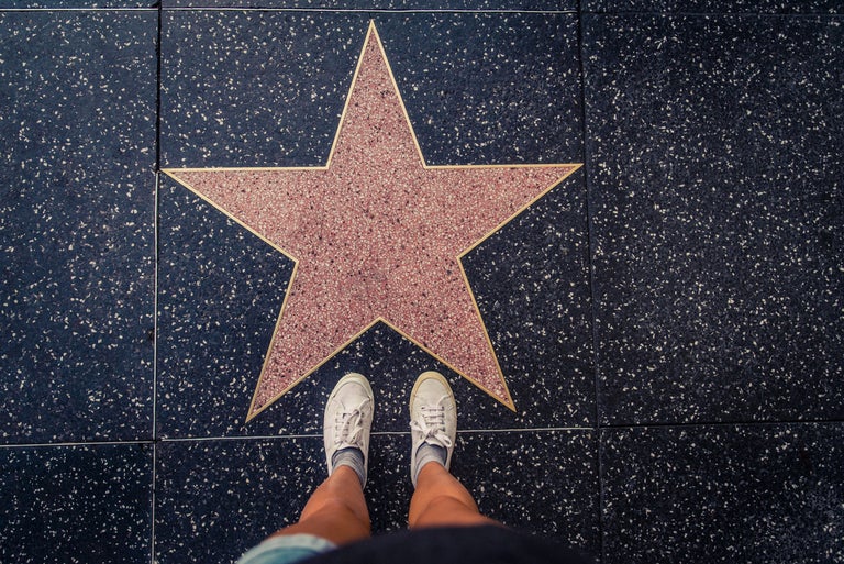 A picture of a person with white shoes standing in front of a star on Hollywood boulevard.