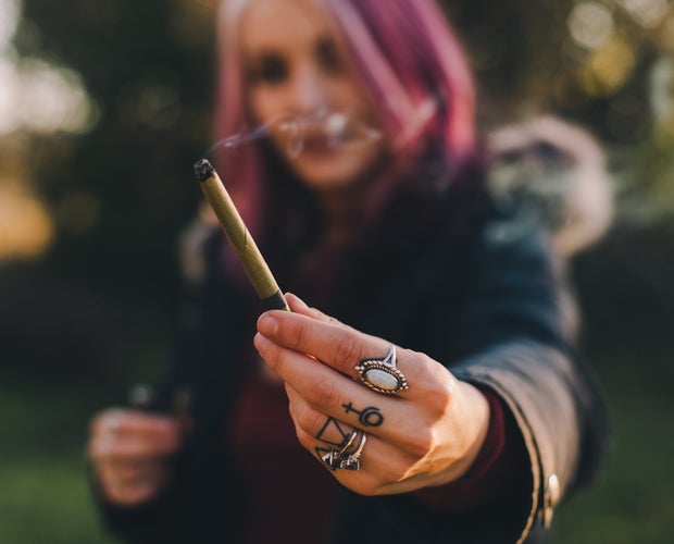 Pink haired woman holding a joint of weed in her hand.
