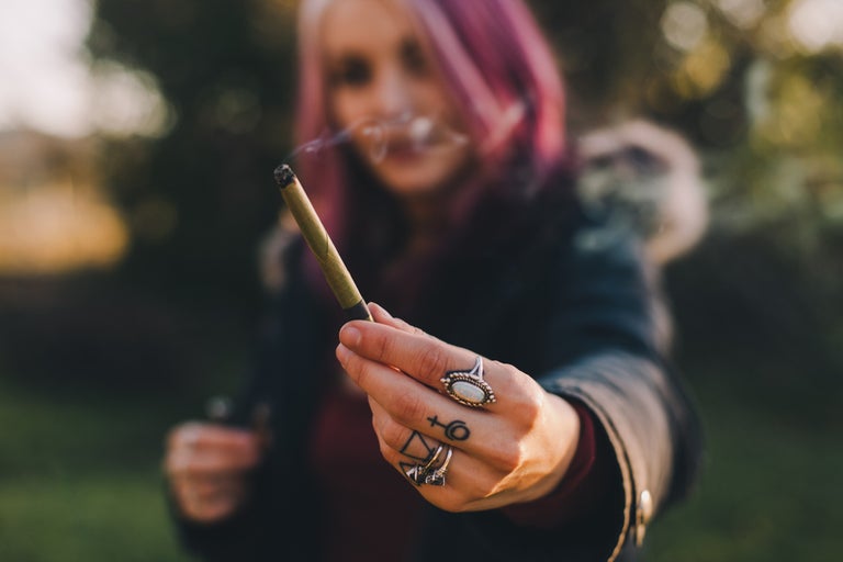 Pink haired woman holding a joint of weed in her hand.