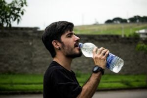 Male in 20s drinking from a large plastic water bottle to refuel.