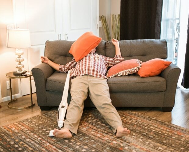 Middle-aged man sleeping on couch after smoking too much weed. He is in deep sleep with his arms and legs spread out wide with a pillow on his face.