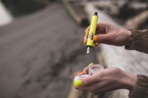 Woman holding a yellow pencil-like dab rig in one hand and concentrates in the other.