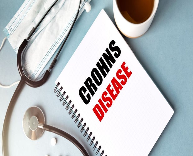 Featured image for an article on cannabis for Crohn's disease. A textbook with the text Crohn's disease sits on a desk next to medical equipment.