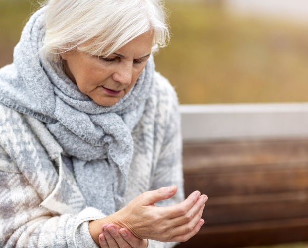 Elderly lady sitting on a wooden bench suffering from arthritis and holding her hand.