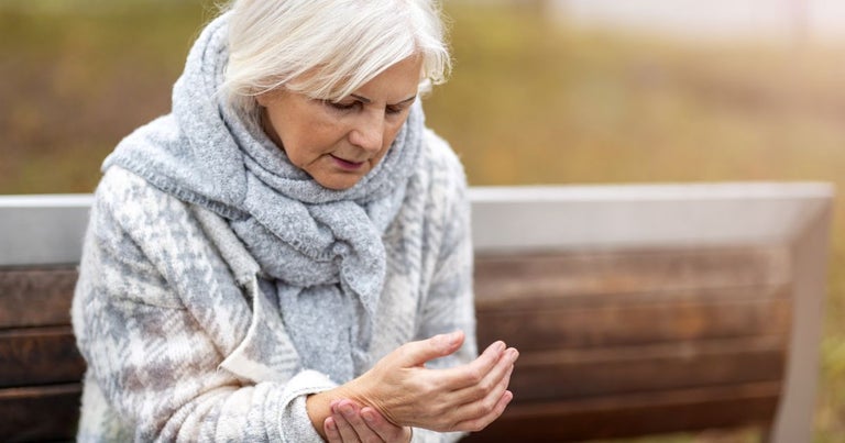 Elderly lady sitting on a wooden bench suffering from arthritis and holding her hand.