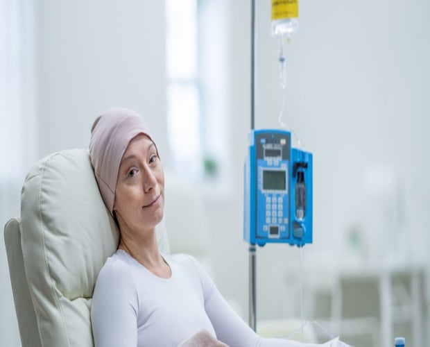 Middle-aged woman in a hospital bed. She is going through chemotherapy and has a cap on.