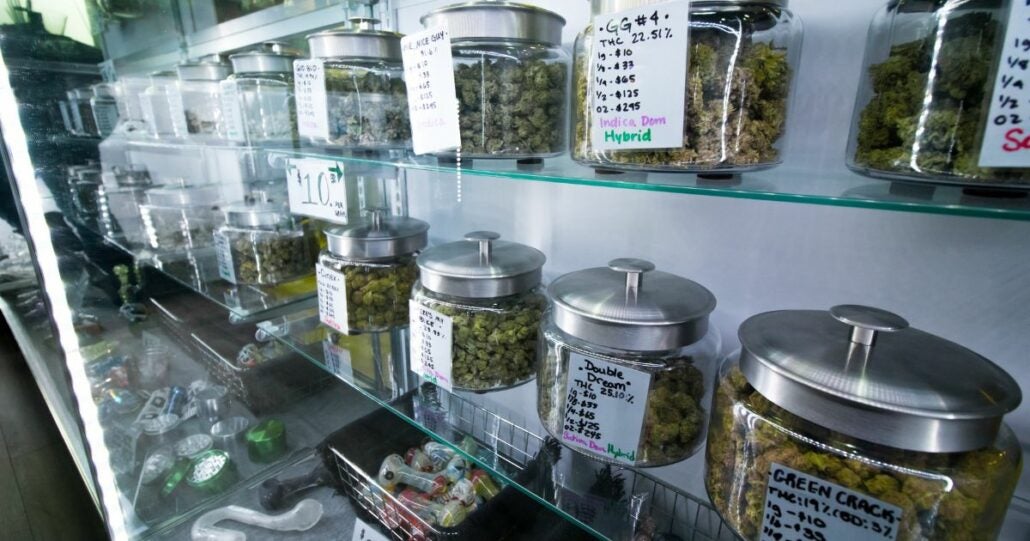 A shelf full of cannabis buds, each held in a glass jar.
