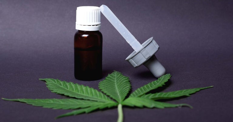 CBD oil glass bottle with syringe cap and marijuana leaf under it.