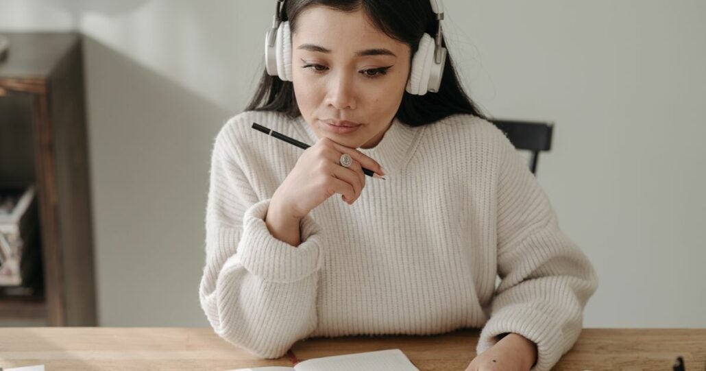 Young woman wearing headphones with a pencil and notebook in front of her.