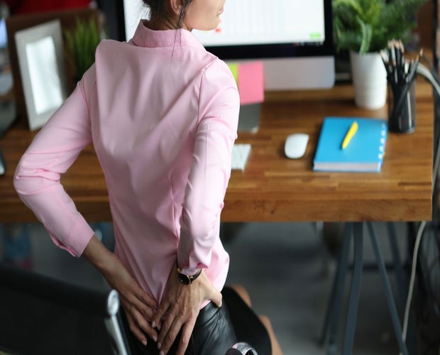 Cannabis for pain management blog featured photo. A young woman is sitting at a desk holding her back.