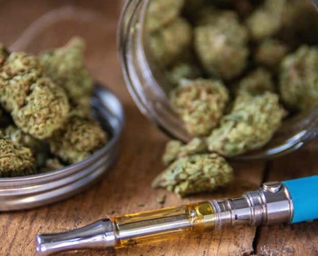 Cannabis Vape pen on a wooden desk next to cannabis buds.