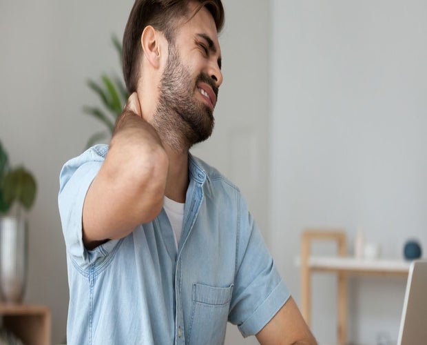 Young adult male suffering from fibromyalgia, holding his neck and squinting.