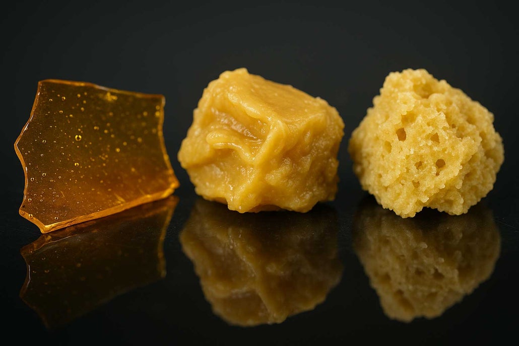 Macro close-up of shatter, wax, and crumble cannabis concentrates side by side on a glossy black glass surface, showcasing their unique textures, colors, and details under studio lighting.
