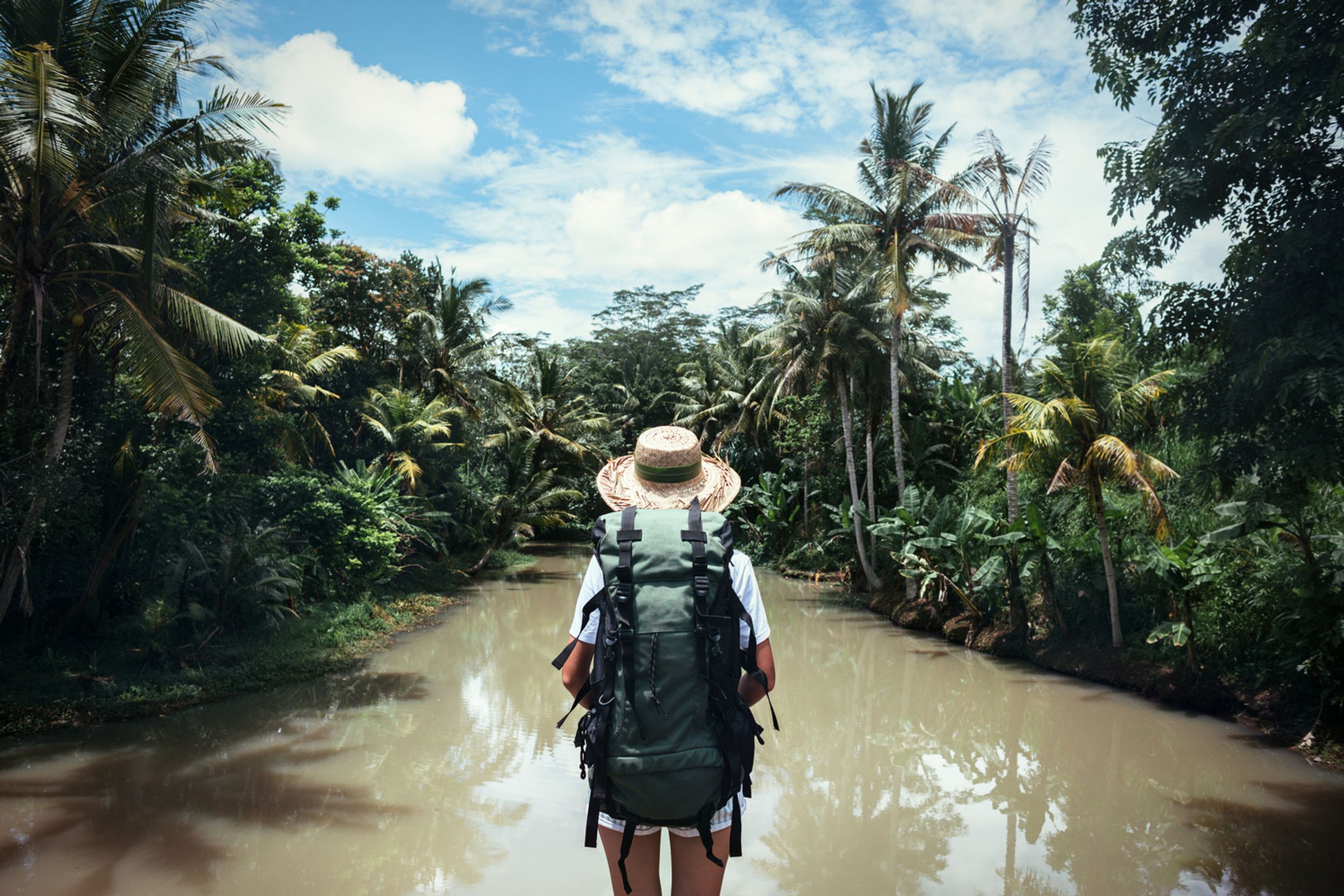 Traveling woman with a large backpack in a tropical river blue sky and white clouds