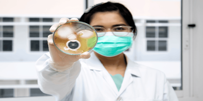 woman with mask holding mold in glass container