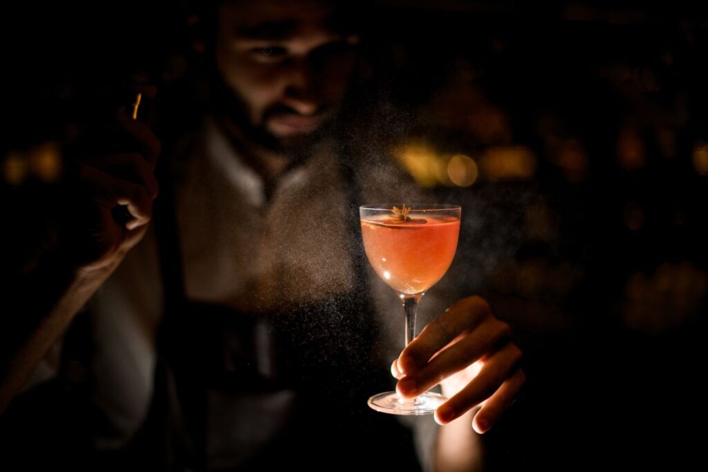 THC syrup added to red cocktail in wine glass. Young man proudly holding it with one hand.