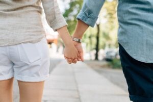 A picture of a couple holding hands and walking down a street.
