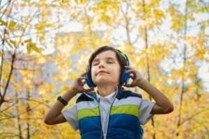 A picture of a young child listening to music in a yellow forest.