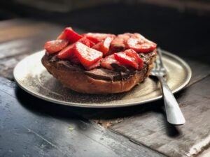 A picture of a snack that is made from a piece of bread with Nutella and strawberry on top.