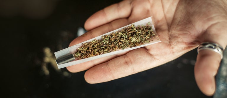 A hand holding up a half rolled joint with a black filter on the end of it.