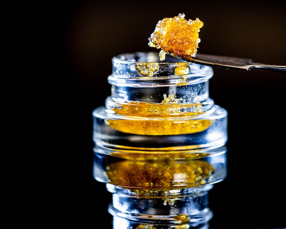 Live Resin in a glass container. An orange sticky substance that looks like salmon row is scooped up with a spoon.