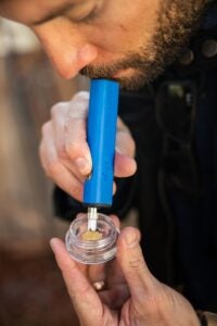 Blue concentrate vape. Young male presses down on live resin with his vape to enhale it.