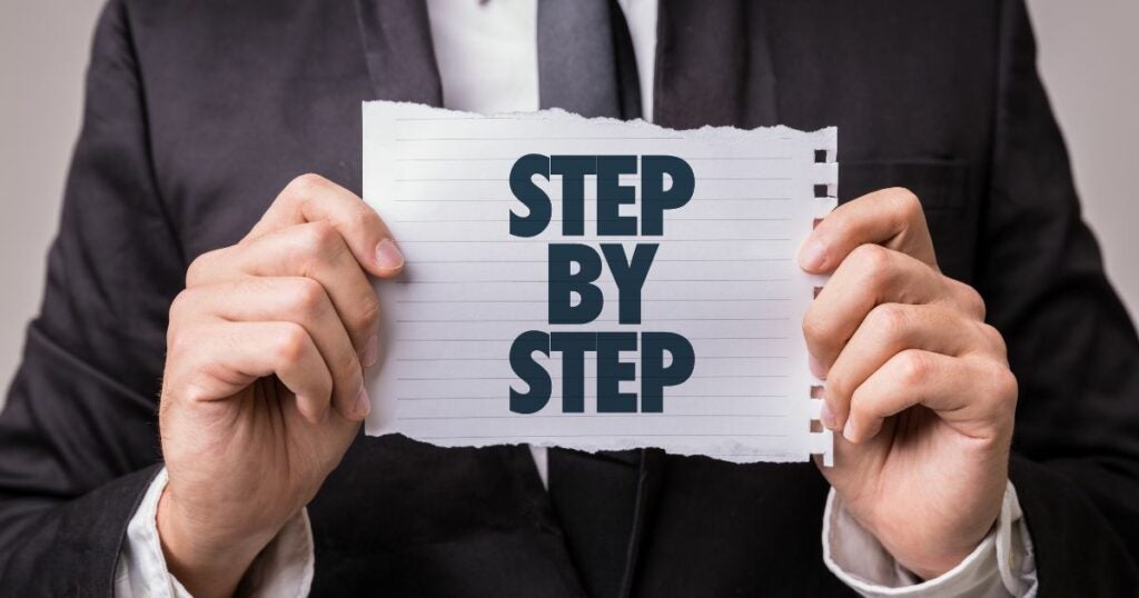 Man in black suit, holding up a sign that reads "Step by Step".