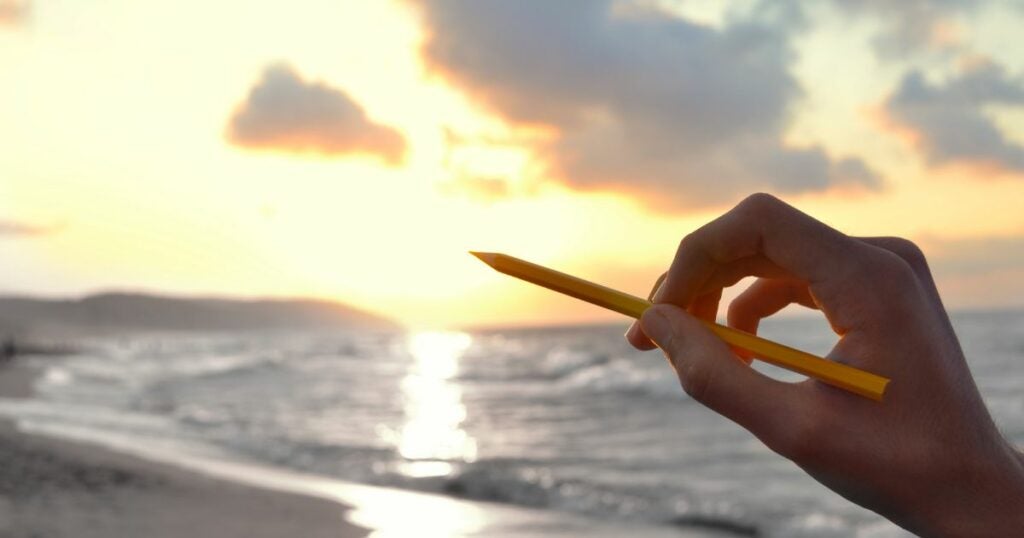 Artist with a pencil in hand is getting creative inspiration to draw from the ocean scenery.