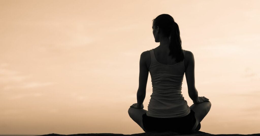Young lady sitting infront of a beautiful sunset. She is in a meditative pose relaxing.