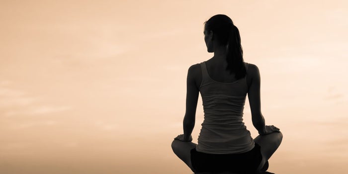 Young lady sitting infront of a beautiful sunset. She is in a meditative pose relaxing.