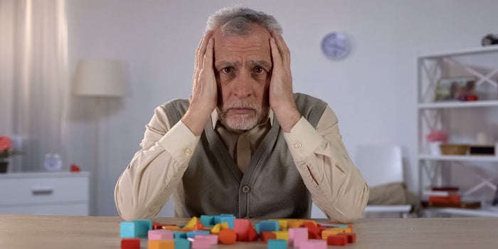 Elderly man suffering from Alzheimer's disease. He is holding his head with both hands and looking towards the camera.