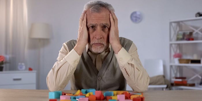 Elderly man suffering from Alzheimer's disease. He is holding his head with both hands and looking towards the camera.