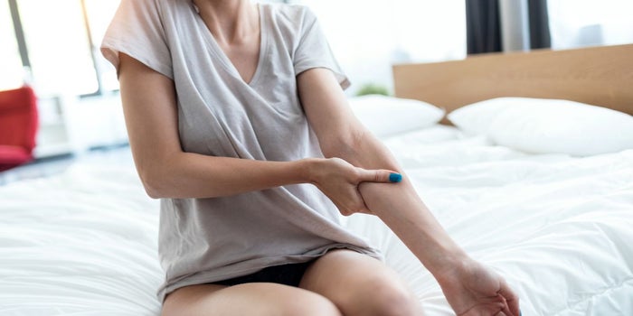 Young female patient suffering from Fibromyalgia. She is sitting on a bed, holding her arm.