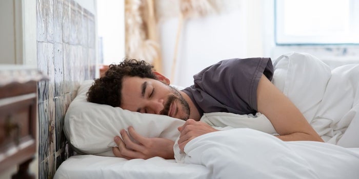 Young man sleeping well in a bed with with blankets and a pillow.