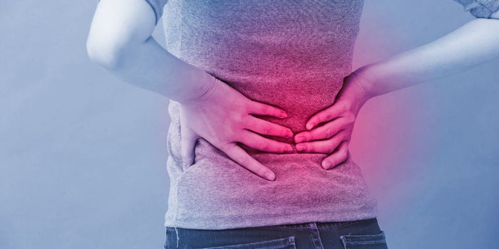 Woman holding back due to injury. The lower back area that is affected is highlighted in red.