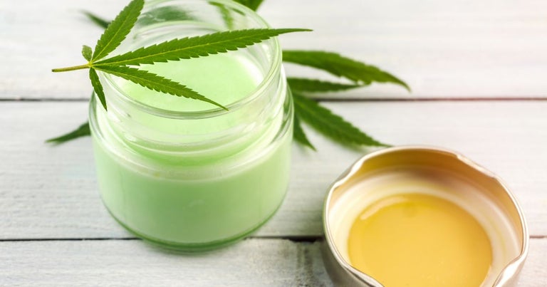 Cannabis topical cream in a glass jar on a white wooden bench.