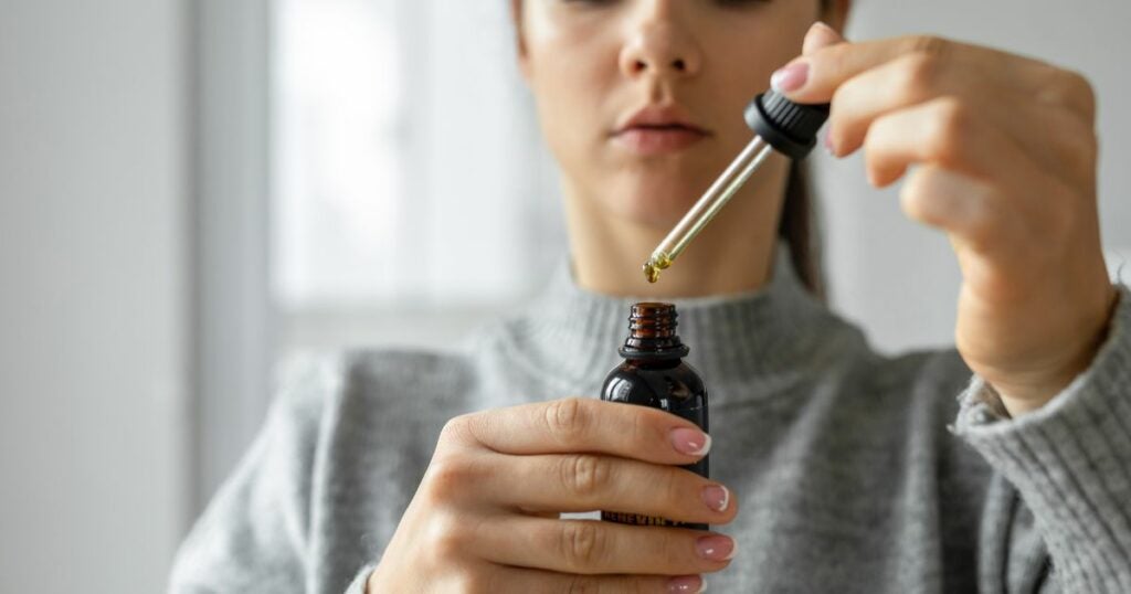 young woman extracting cannabis oil from bottle.