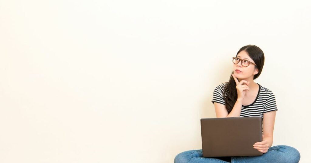 Young woman thinking carefully with a laptop on her lap.