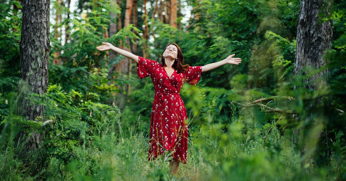 A young woman standing in nature with her arms spread out.