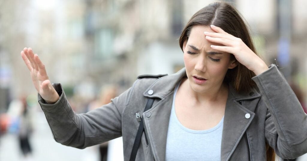 Young Caucasian woman visibly dizzy and holding her head. 