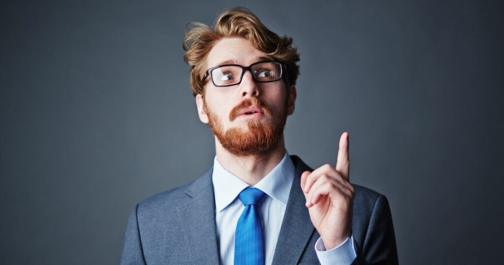 Young man in a suit and glasses pointing a finger up to provide a solution.