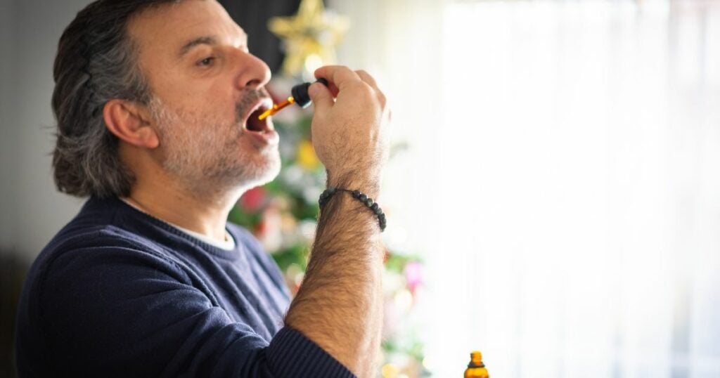 Elderly man with long hair ingesting CBD oil through his mouth.