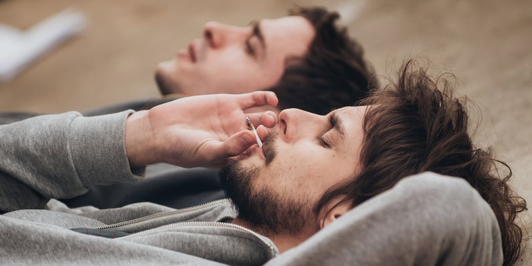 2 caucasian friends lying down while enjoying a joint.