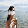 Young stylish woman vaping THC vape pen on the beach.